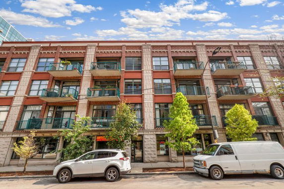 Front view of a four-story apartment building with balconies and parked cars.