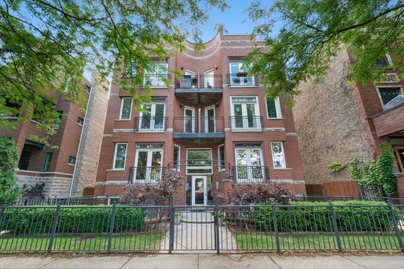 Front view of a multi-story brick residential building with balconies and a gated entrance.