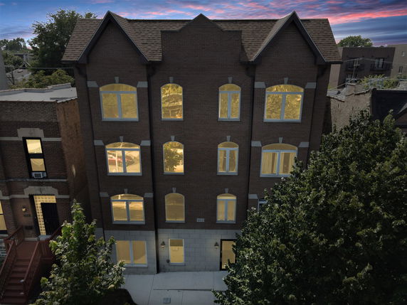 Front view of a multi-story brick building with illuminated windows.