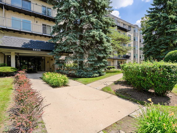 Front view of a multi-story building with balconies and a pathway leading to the entrance.