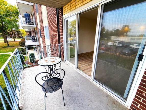 View from a balcony with a small table and chair, overlooking parking and neighboring balconies on a multi-story building.