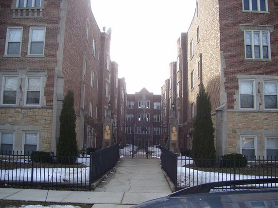 Front view of a multi-story brick apartment building with a gated entrance.