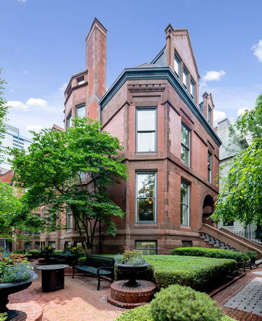 Front view of a multi-story brick house with large windows and chimneys.