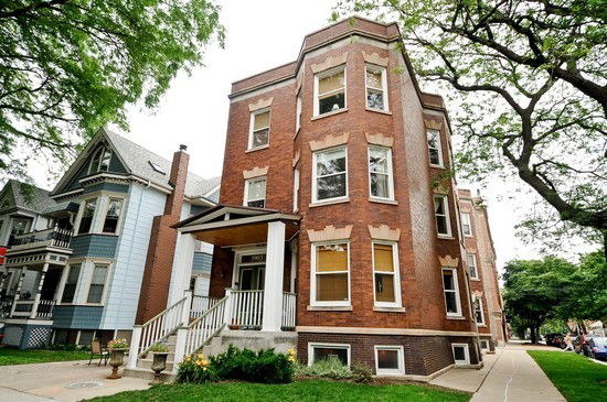 Front view of a multi-story brick building with a porch and stairs.