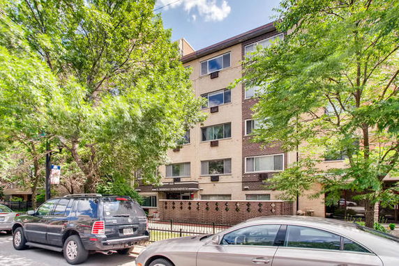 Front view of a multi-story residential building with trees and parked cars in front.