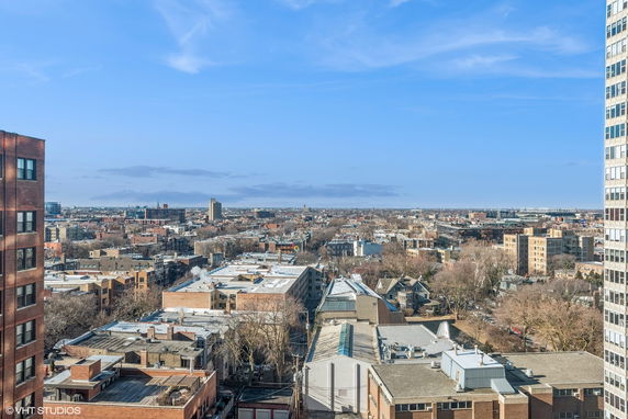 Panoramic view of a cityscape with multiple buildings and trees under a blue sky.