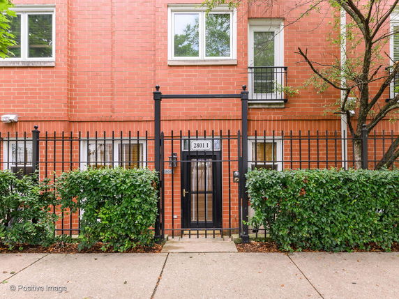 Front view of a brick building with metal fencing and green shrubbery.