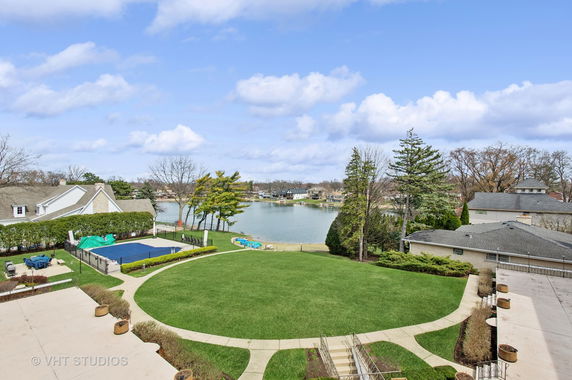 Panoramic view of a landscape with a lake, landscaped area, and several houses in the background.