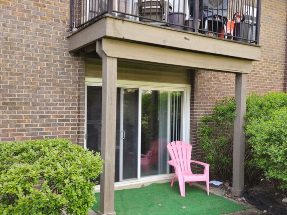 View of a patio area with a sliding glass door and overhanging balcony.
