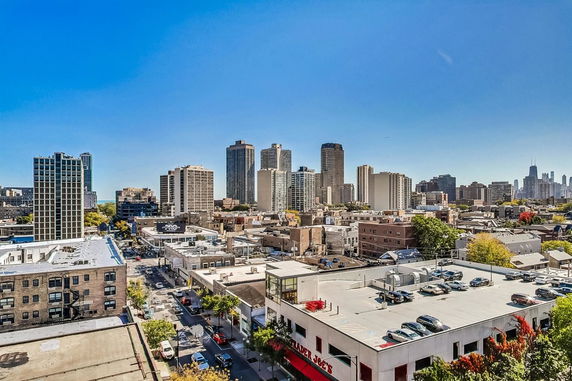 Panoramic view of a city skyline with multiple high-rise buildings and a parking lot on a sunny day.