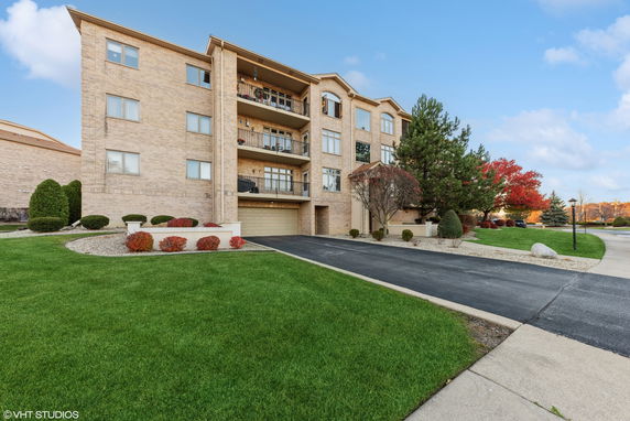 Front view of a multi-story brick apartment building with balconies and a driveway.