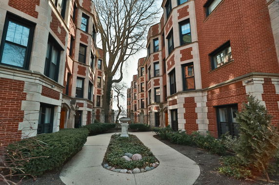 Front view of a multi-story red brick apartment building with landscaped pathway.