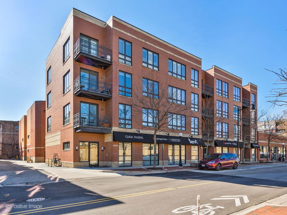 Front view of a multi-story brick apartment building with balconies and storefronts on the ground level.