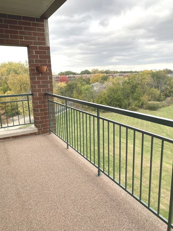 View of a grassy area and trees from a balcony with brick and metal railing.
