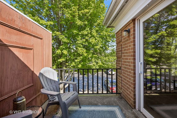 Balcony area with a chair and table, overlooking trees and parked cars.