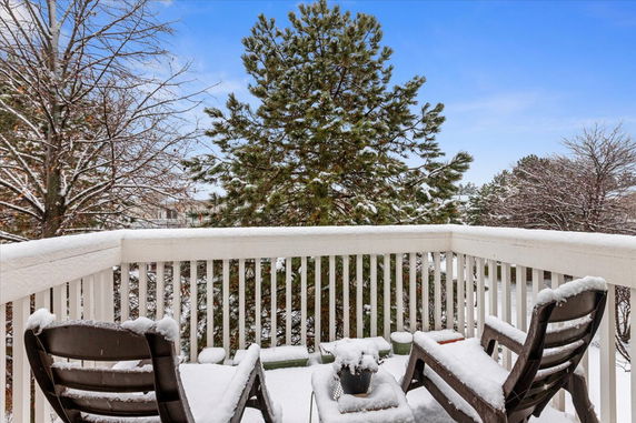 Snow-covered balcony with chairs and a view of trees and sky.