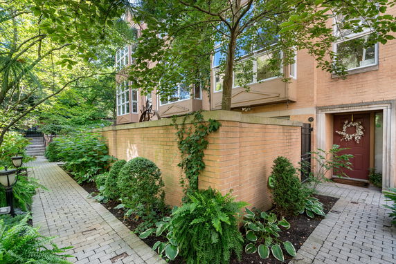 Front view of a house with rectangular bay windows, brick walls, and a pathway surrounded by plants.
