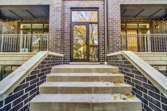 Front view of a building with brick facade and stairs leading to glass door entrance.