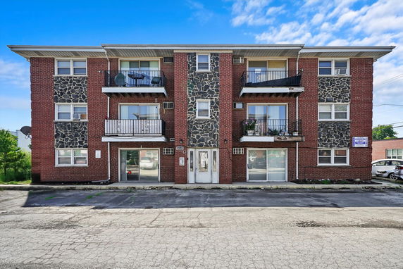 Front view of a three-story brick apartment building with balconies.