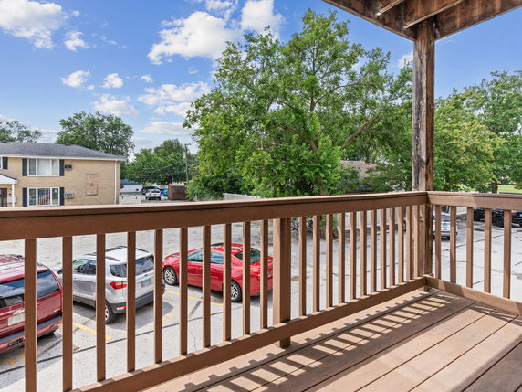 View from a wooden balcony overlooking a parking area with several cars and nearby residential buildings.