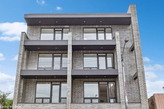 Front view of a three-story brick building with large windows and balcony areas.