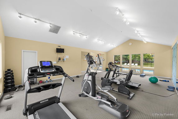 Interior view of a gym with exercise equipment and windows looking out to a pool.