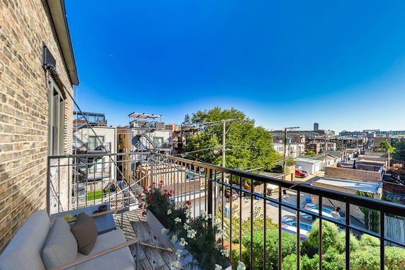 Panoramic view from a balcony showing urban rooftops and a clear blue sky.