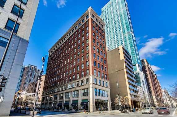 Front view of a multi-story brick building with numerous windows and a modern high-rise adjacent.