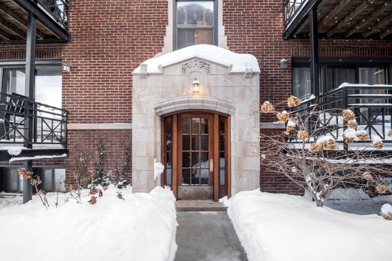 Front view of a brick building entrance with a stone arch and snow-covered surroundings.