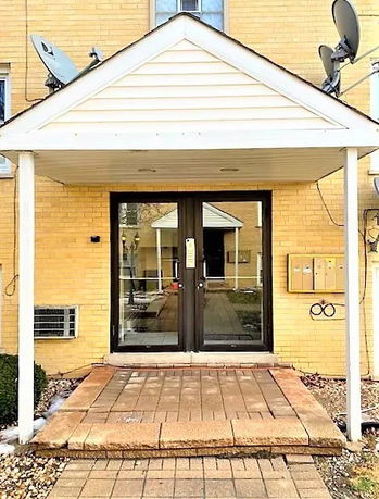 Front view of an entryway with a covered porch and glass doors on a brick building.