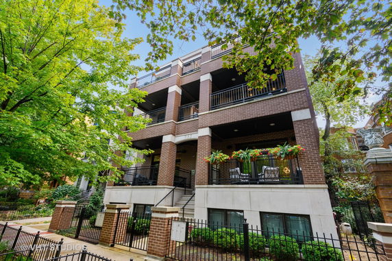 Front view of a multi-story brick building with balconies and decorative plants.