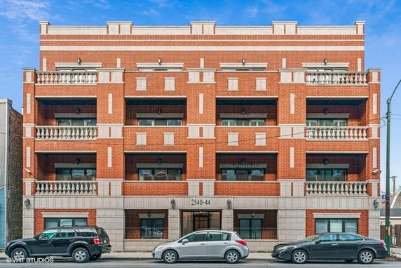 Front view of a three-story brick apartment building with balconies.