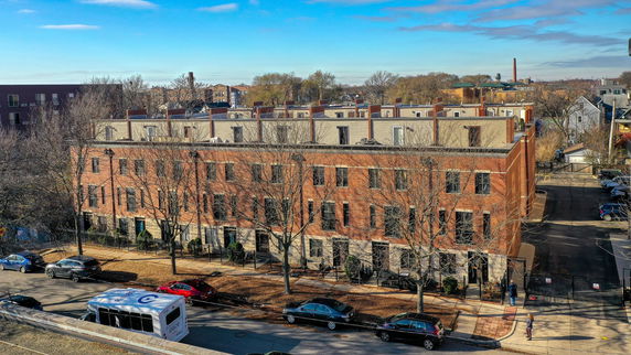 Front view of a multi-story brick building with trees and cars in front.