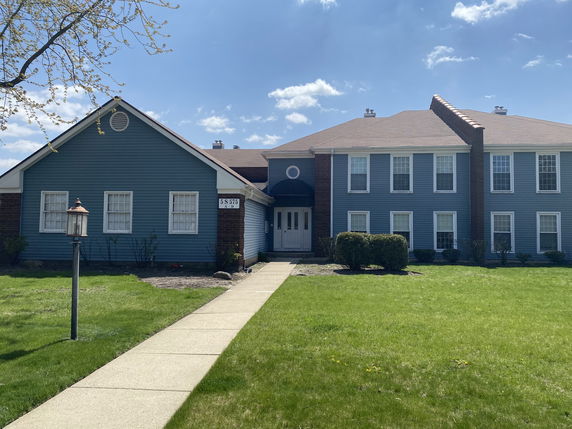 Front view of a two-story blue building with a central entrance and well-manicured lawn.
