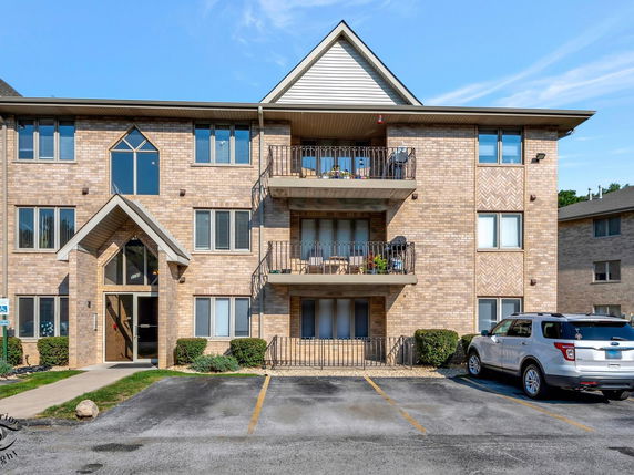 Front view of a three-story apartment building with balconies and parking area.