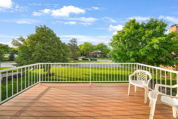 View from a balcony overlooking a tree-lined street and grassy area.