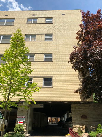 Front view of a multi-story brick building with parking area below.