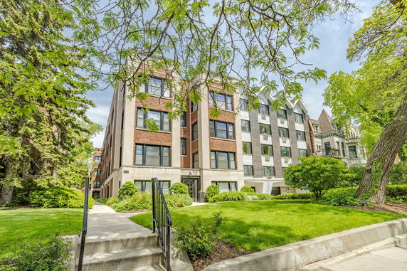 Front view of a multi-story residential building with a walkway and landscaped greenery.