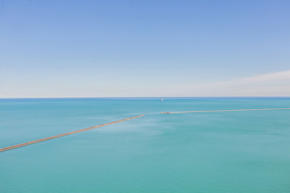 Wide angle view of a calm sea with a distant horizon under a clear blue sky.