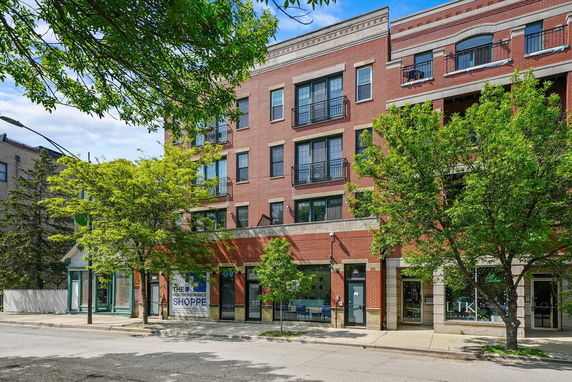 Front view of a multi-story brick building with balconies and commercial spaces on the ground floor.
