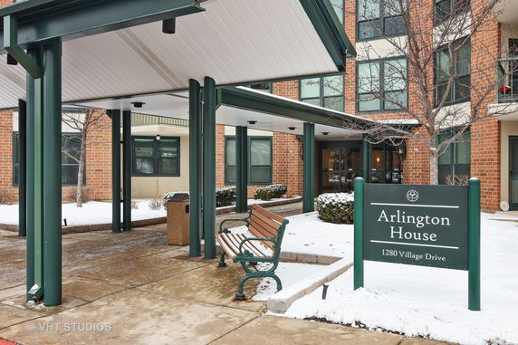 Front view of a multi-story building entrance with a covered walkway and benches.