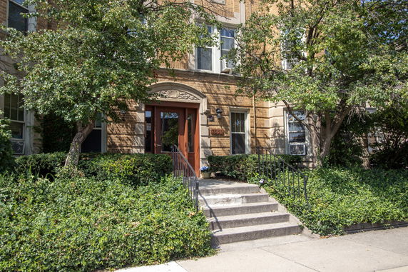 Front view of a multi-story brick building with a central entrance and surrounding greenery.