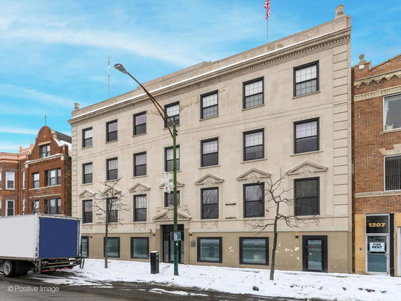 Front view of a multi-story building with symmetrical windows and a flag on top.