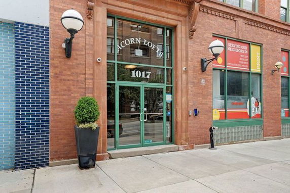 Front view of a brick building entrance labeled 'Acorn Lofts' with large glass doors and decorative lighting.