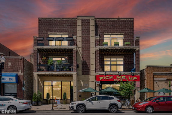 Front view of a brick building with balconies and street-level businesses.