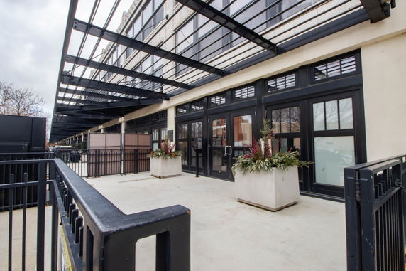 Front view of a building with large windows and metal overhang, featuring decorative plant arrangements.