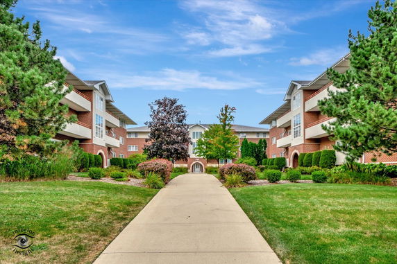 Front view of a multi-story brick building with balconies and a central walkway leading to the entrance.