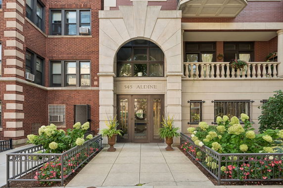 Front view of a multi-story brick building with decorative entrance and potted plants.