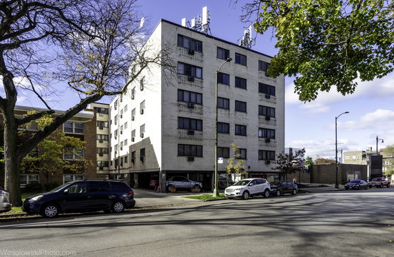 Front view of a multi-story apartment building with parking below and rooftop antennas.
