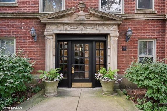Front view of a brick building entrance with decorative stone elements and glass doors.